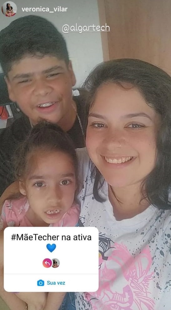 Na imagem vemos uma mulher branca de cabelos escuros com duas crianças, uma menina e um menino. 