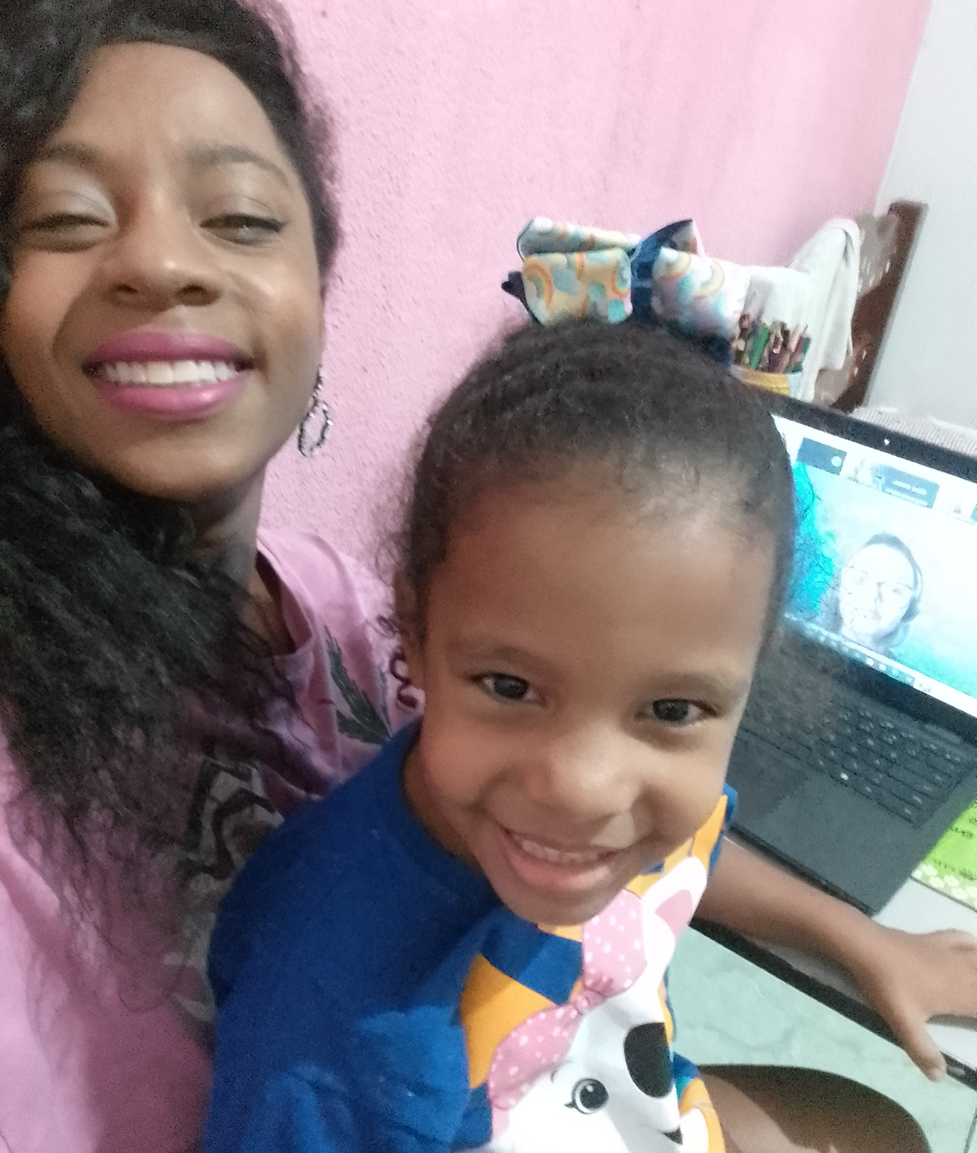 Na imagem vemos uma mulher negra com uma blusa rosa com uma menina no colo. 