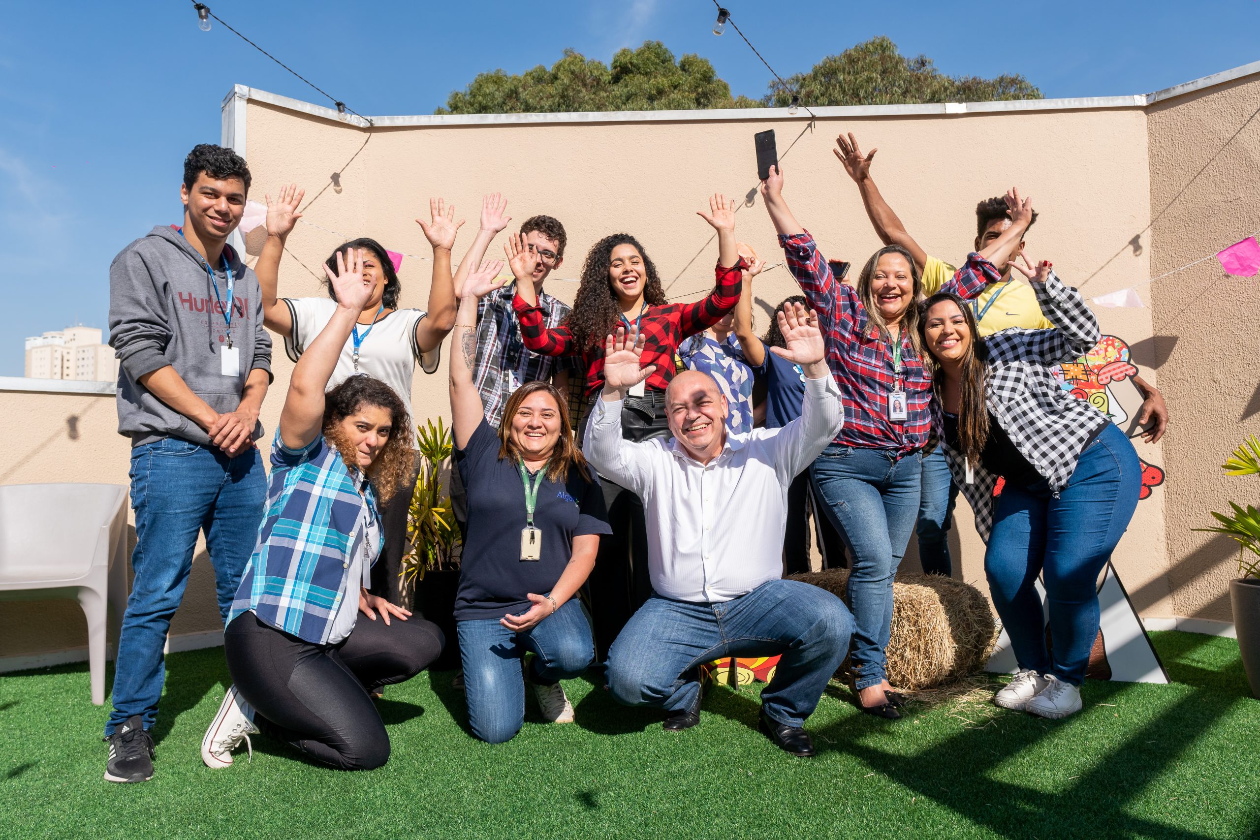 Na imagem vemos um grupo de pessoas animadas posando para foto em um local aberto com grama no chão.