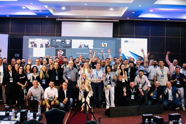 Na imagem vemos vários executivos, alguns de pé outros agachados posando para foto sorrindo em uma sala de conferencias.